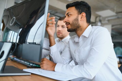 Two men traders sitting at desk at office together looking at data analysis discussing brainstorming successful strategy inspired teamwork concept close-up Two men traders sitting at desk at office together looking at data analysis discussing brainstorming successful strategy inspired teamwork concept close-up