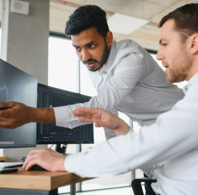 Two successful trader in formalwear pointing at display, analyzing stat and dynamic on forex charts, working in office together
