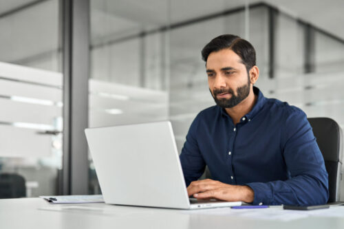 Busy Indian business man employee looking at laptop working at desk in office. Busy Indian business man employee looking at laptop working at desk in office.
